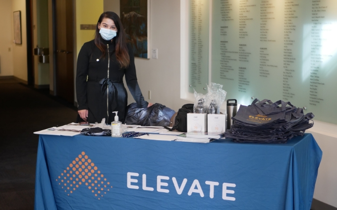 Person standing behind a table with materials and a tablecloth that says Elevate