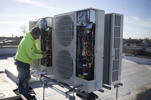 Person installing a heat pump unit on a rooftop.